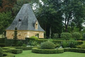 Topiaires de buis taillés devant un pavillon au toit de lauzes dans les jardins d'Eyrignac