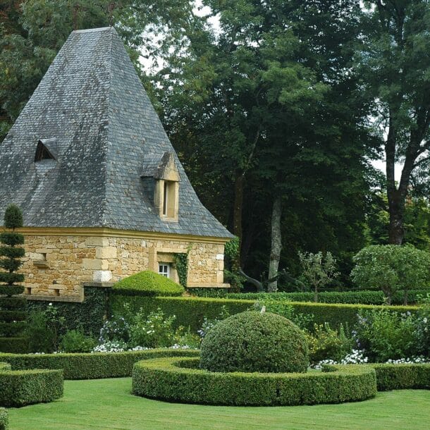 Topiaires de buis taillés devant un pavillon au toit de lauzes dans les jardins d'Eyrignac