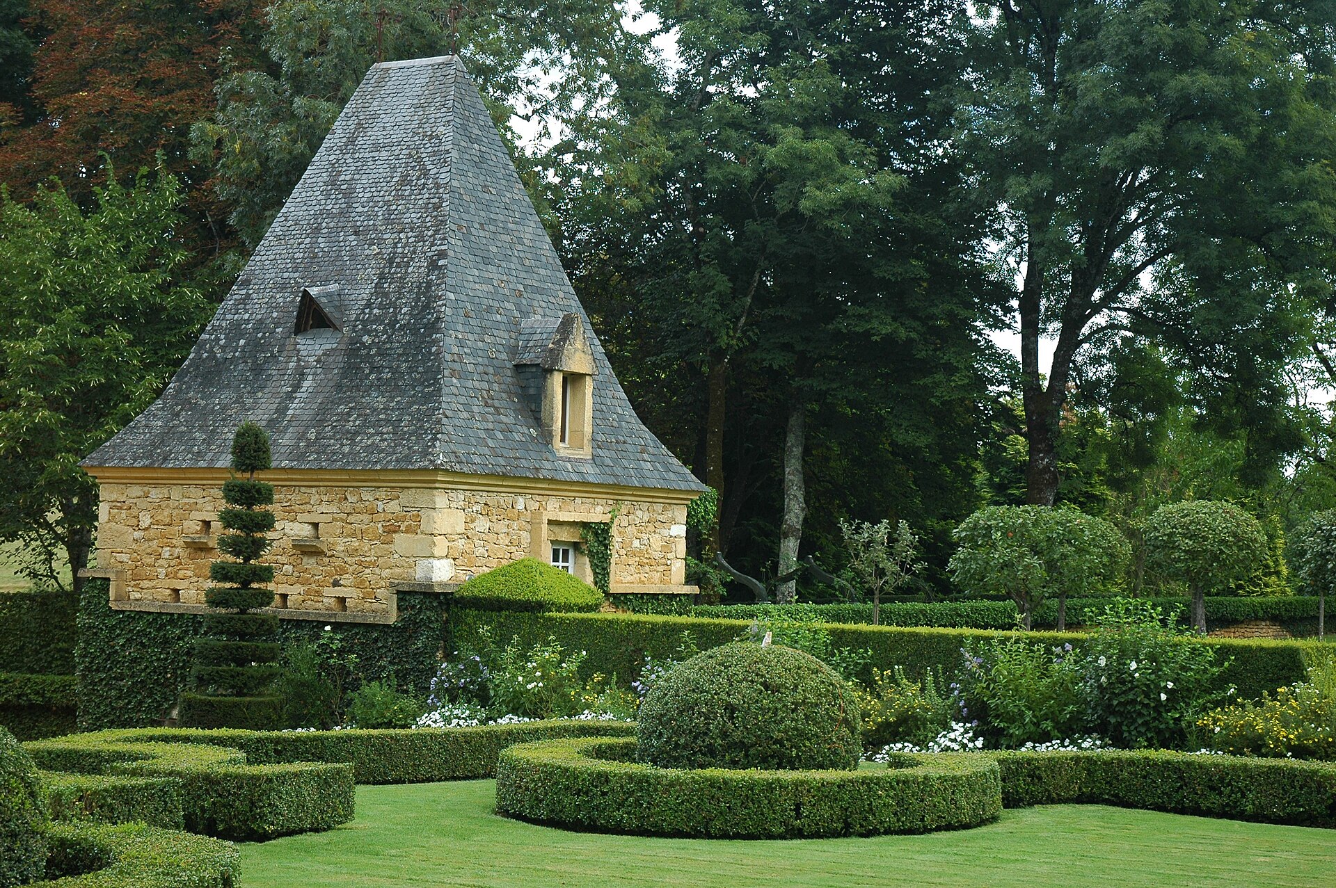 Topiaires de buis taillés devant un pavillon au toit de lauzes dans les jardins d'Eyrignac